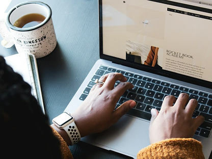 Person writing on a laptop beside a coffee cup